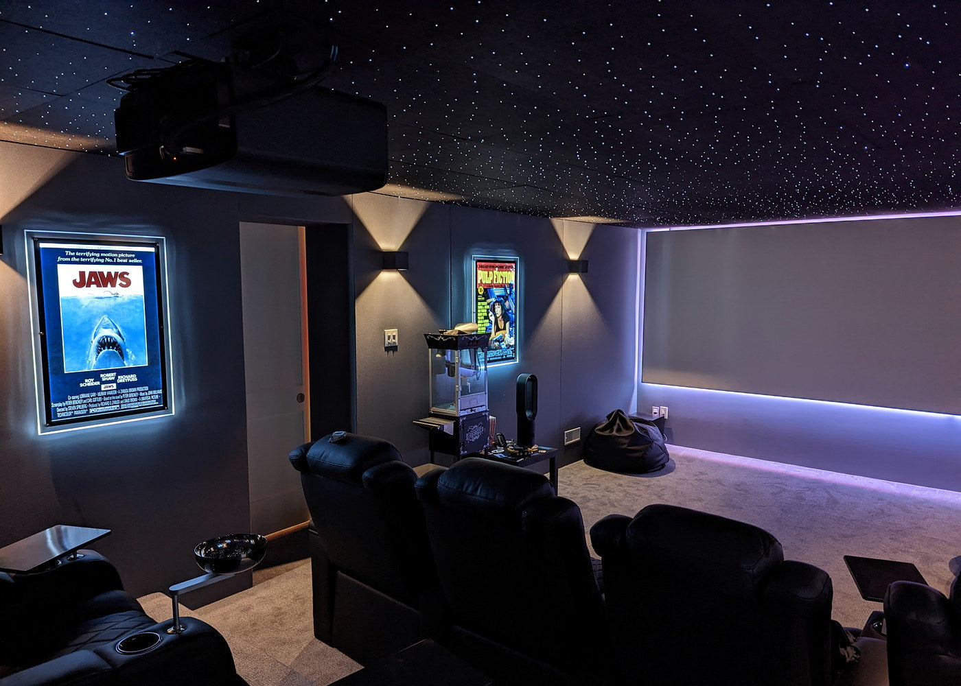 Dark home cinema with recliners, movie posters, a popcorn machine, and a starlight ceiling